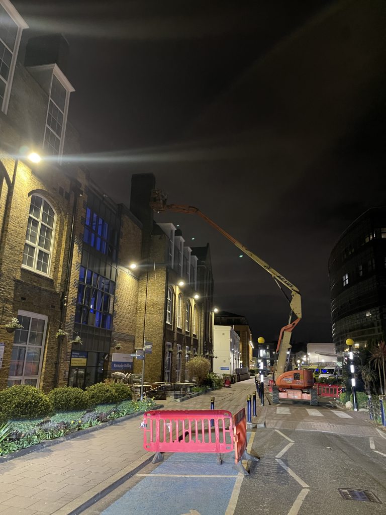 Technician cleaning an industrial roof at night using a MEWP in London.