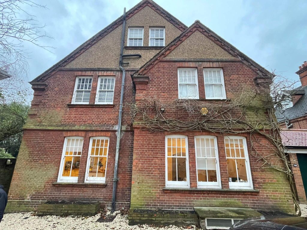 Red brick house in South London with heavy wisteria growth and green algae staining before cleaning.