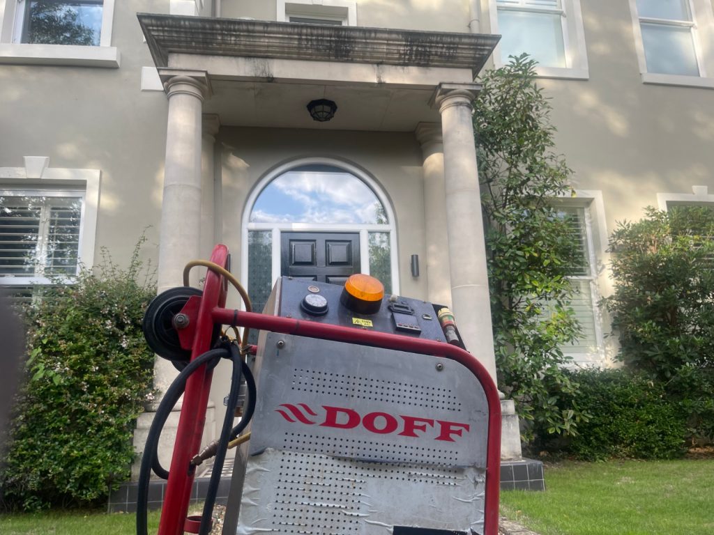 DOFF steam cleaning machine positioned outside residential property with stone columns